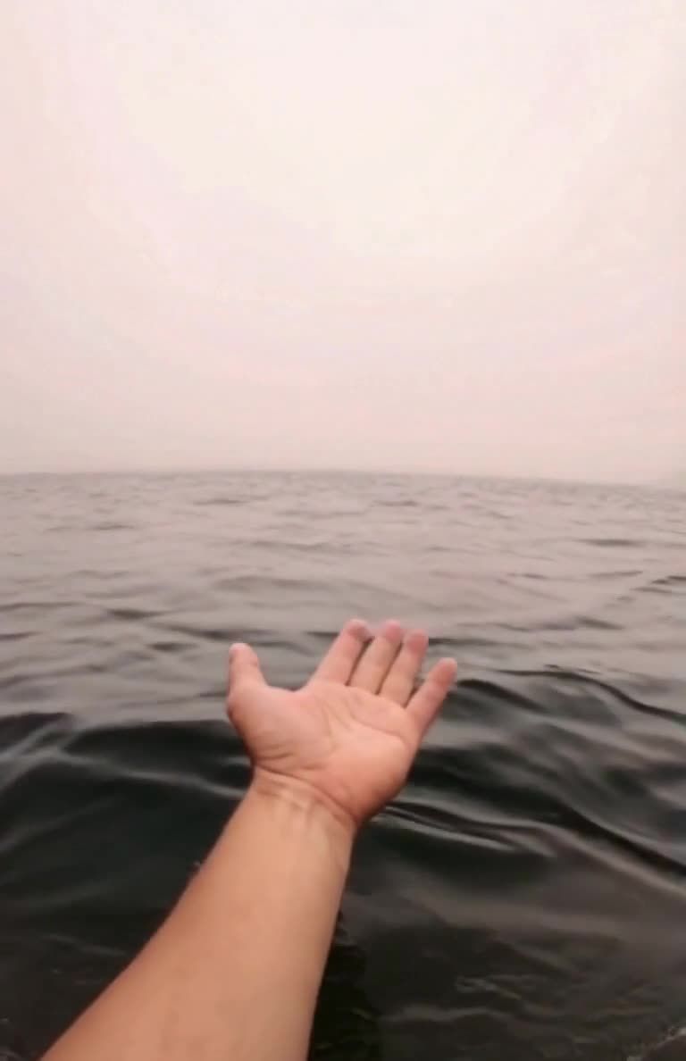 手掌伸向海面，波浪拍打，阴天下的第一视角
