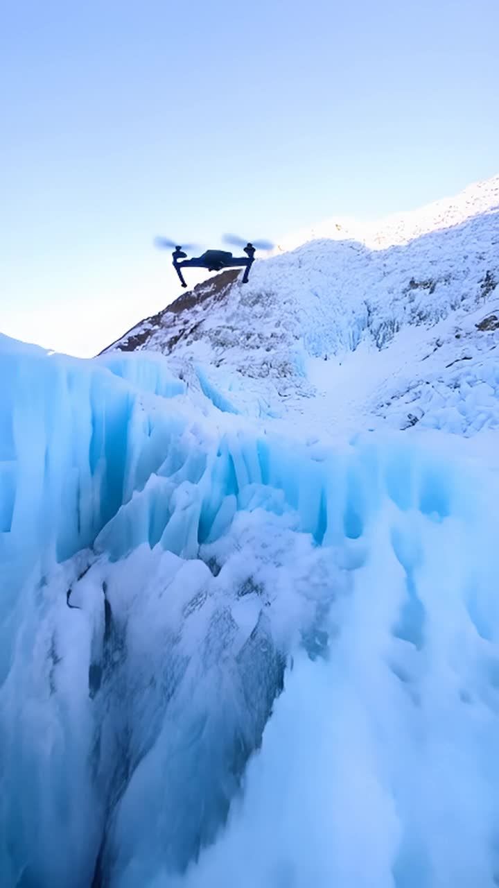 一架无人机正在山脉上空飞行。山脉被冰雪覆盖，呈现出