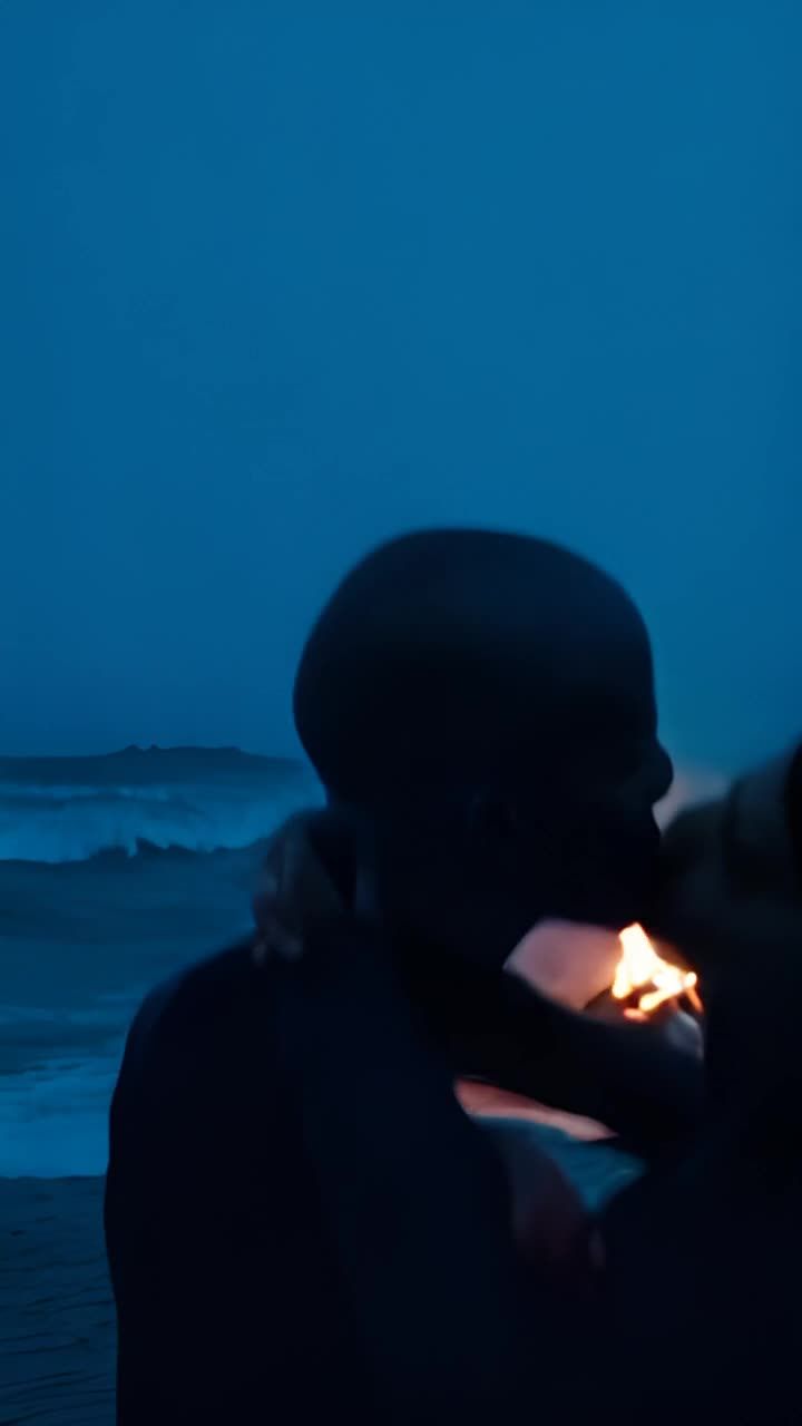 夜晚，海面波涛汹涌，远处有一座灯塔亮着灯光。海滩上