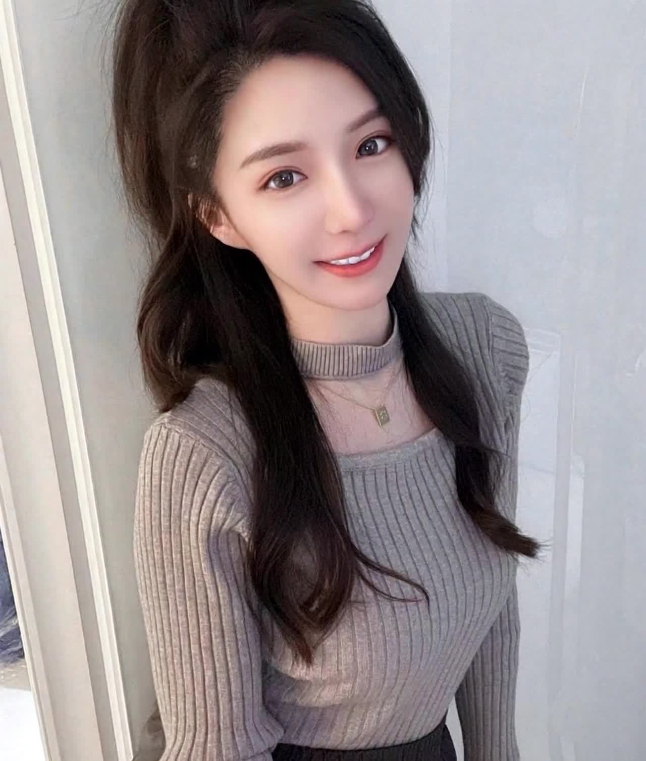 微笑的深发高马尾女性身穿灰色针织衫戴金项链