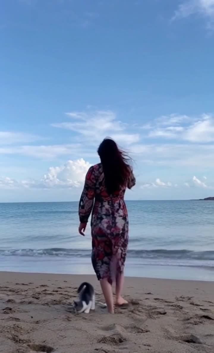 海边沙滩上，海浪拍打着岸边，天空湛蓝。一位穿着花色