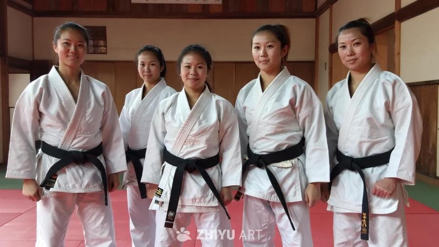 五名女性穿着白色空手道服和黑色腰带，并排站立。她们
