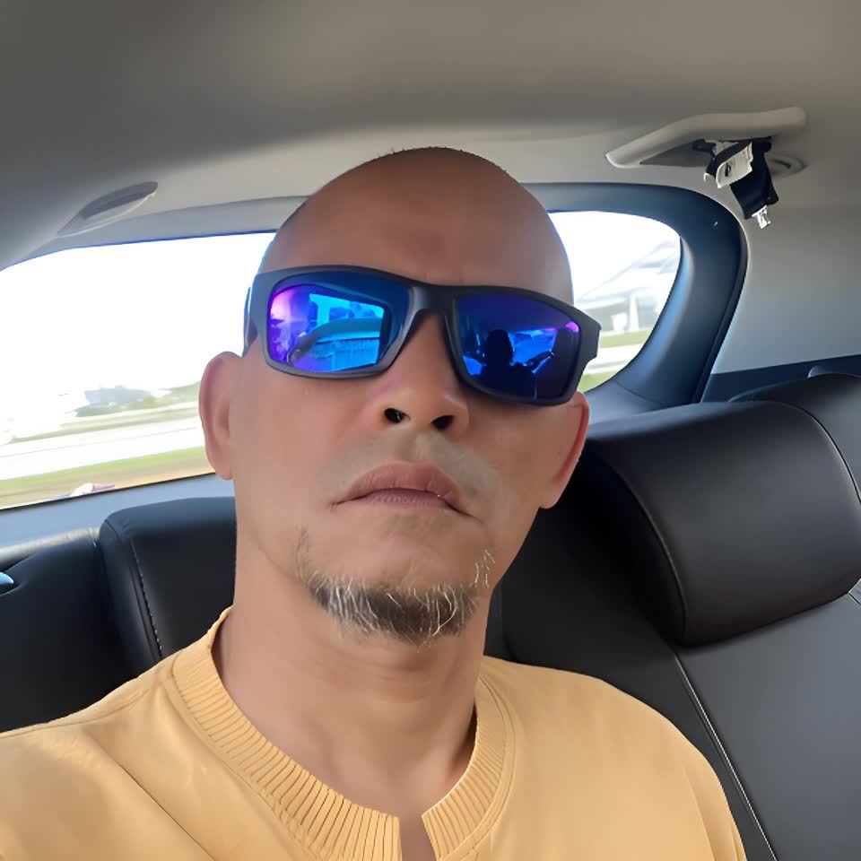 一个戴着蓝色反光太阳镜的秃顶男子坐在汽车后座上。他