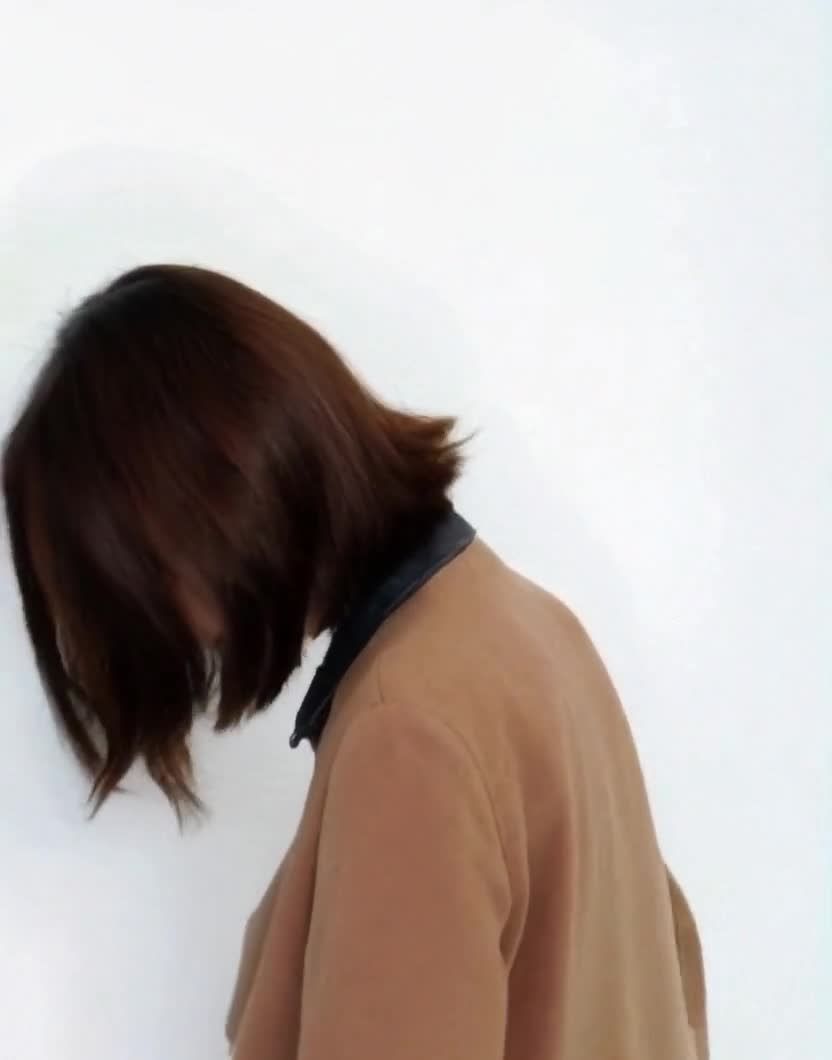 侧身靠墙的女子，棕发外套，低头沉思。