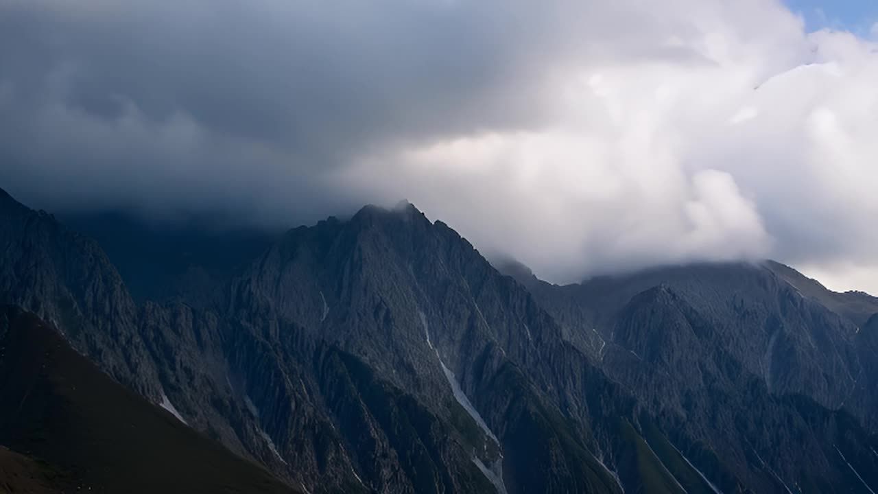 连绵的山脉被云层部分遮盖，山体呈深灰色，部分山坡有