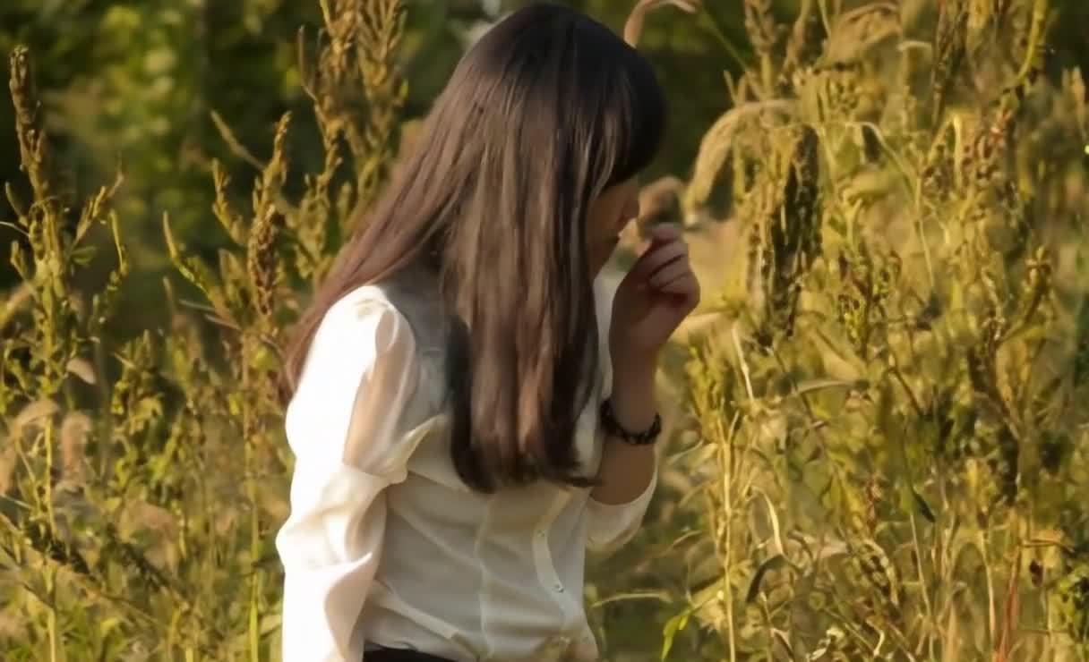 阳光下女子在草丛中闻植物气味。