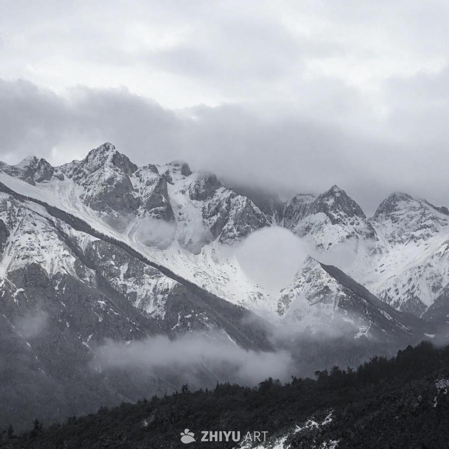 白雪覆盖的山脉在多云的天空下呈现。山体覆盖着一层雪