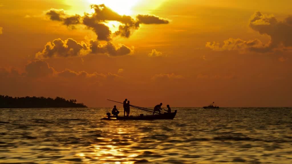 夕阳西下，天空呈现橙黄色，有云朵点缀。海面波光粼粼