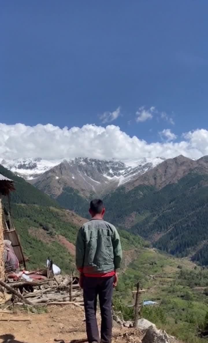 男子山顶眺望雪山，蓝天白云风景壮丽。
