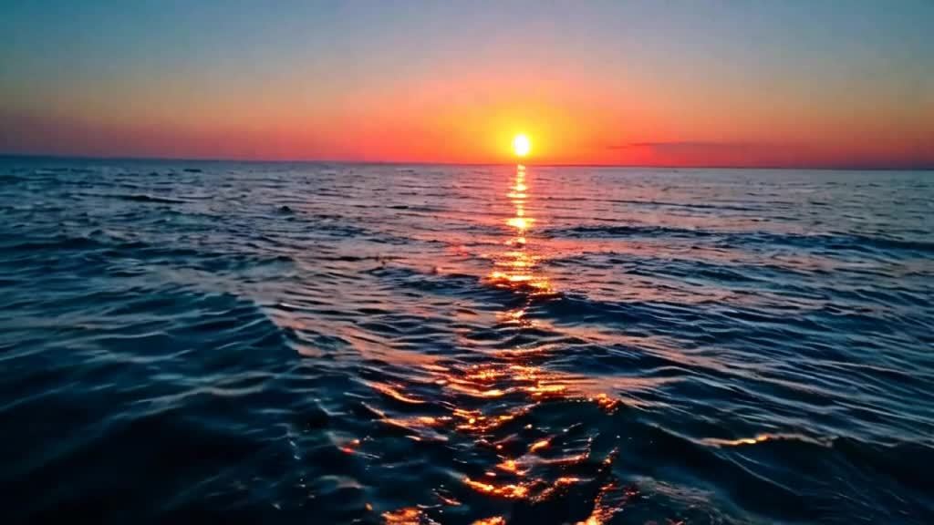 夕阳西下时平静辽阔海洋的景象。天空被描绘成柔和的蓝