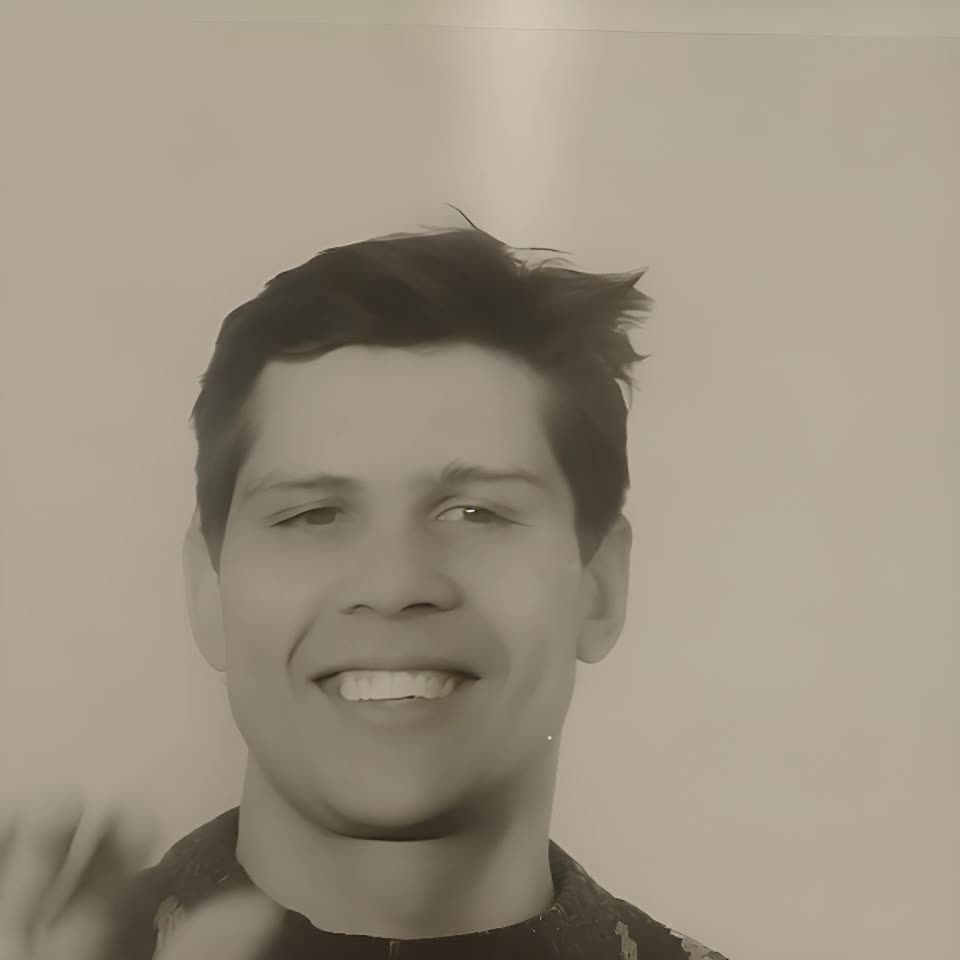 一名男子面对镜头，他的头发是深色的，向上蓬松着，他