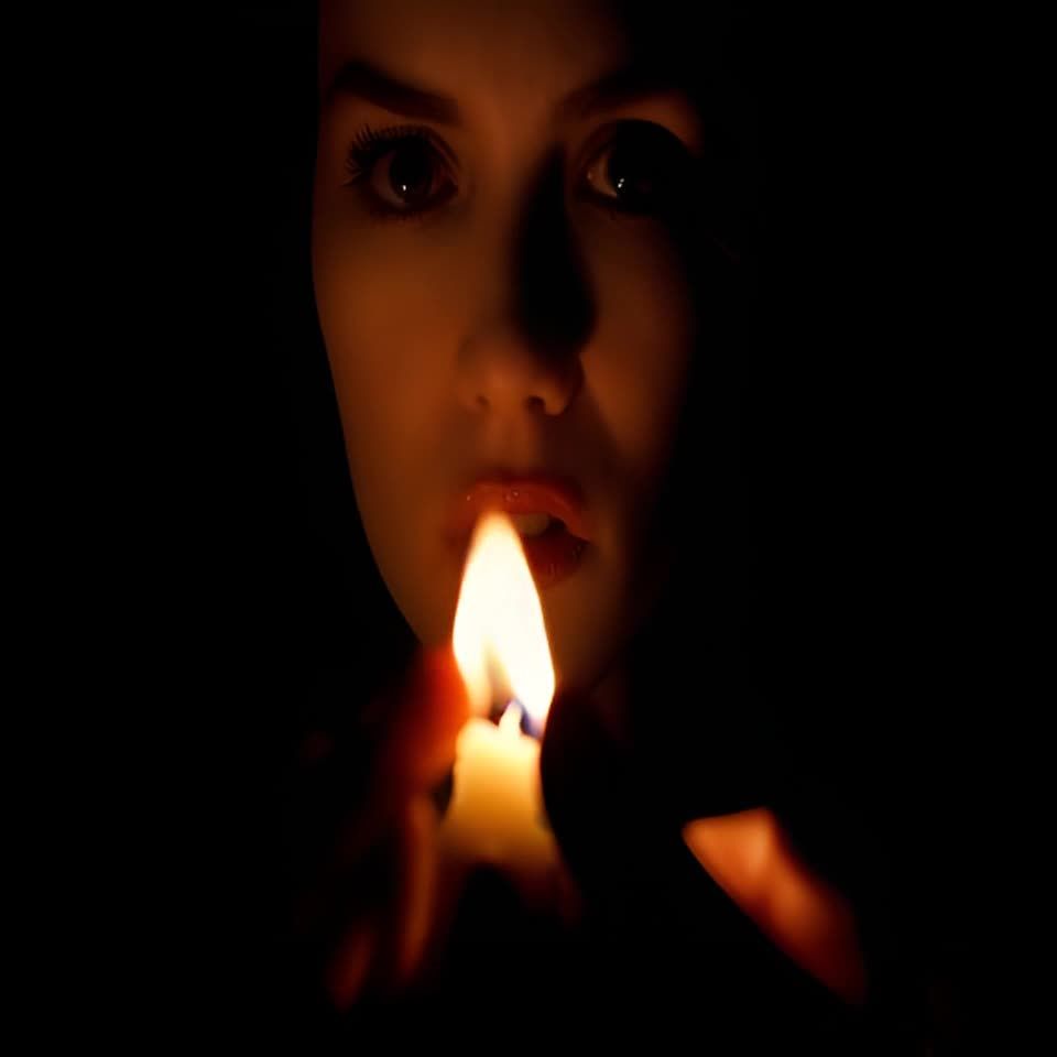 一个女人在黑暗中，手持点燃的蜡烛，蜡烛的火焰照亮了