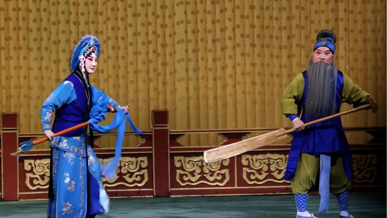 在舞台上，两位京剧演员身着戏服。一位女演员头戴精致