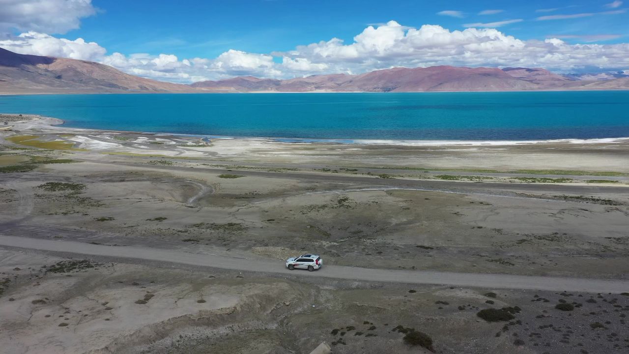 航拍越野车行驶在佩枯错湖边的土路上