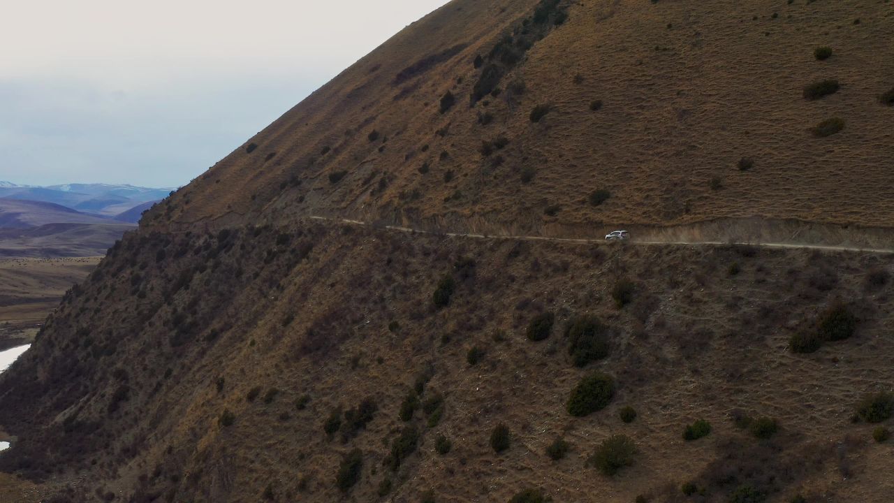 越野车行驶在高原草甸半山腰的土路上