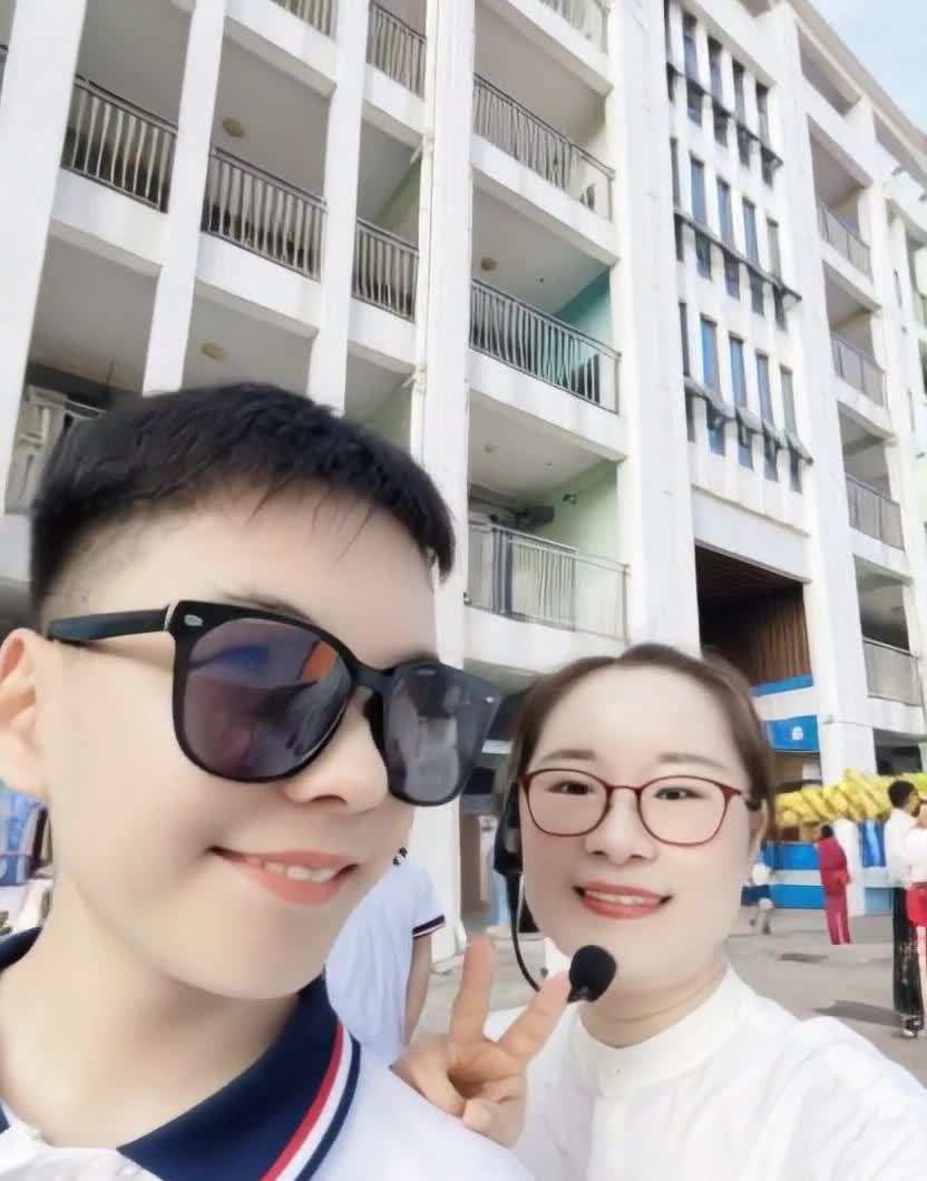一名戴着太阳镜的年轻人在镜头前微笑，旁边站着一位戴