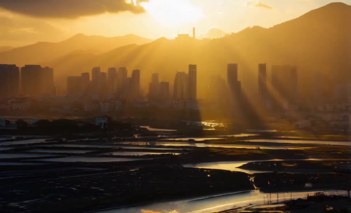 夕阳的光线从山顶倾泻而下，照亮了远处的城市。城市中