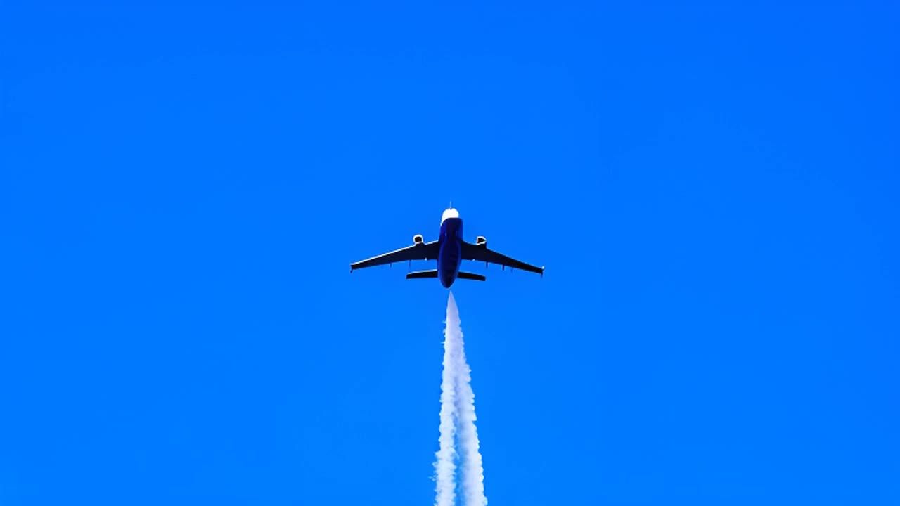 一架飞机在天空中翱翔，尾部留下两条凝结尾迹，背景是