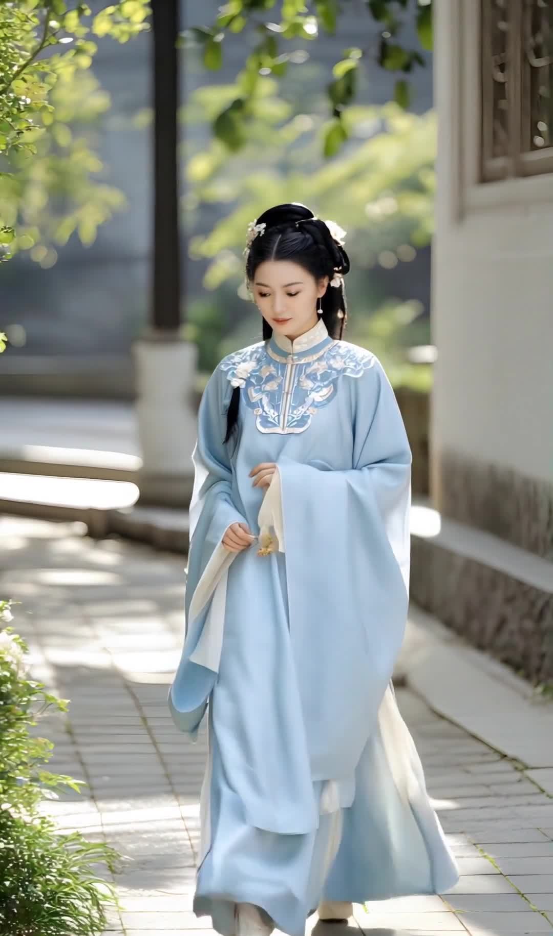 一位身着浅蓝色传统服饰的女子站在铺有石板的小路上。