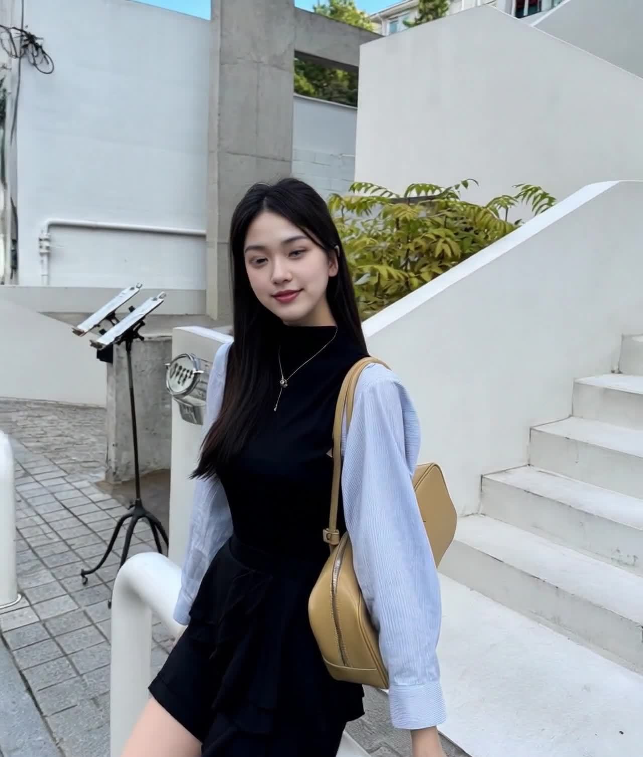 微笑女性，黑衣短裙蓝衬衫，米色包，户外台阶绿植
