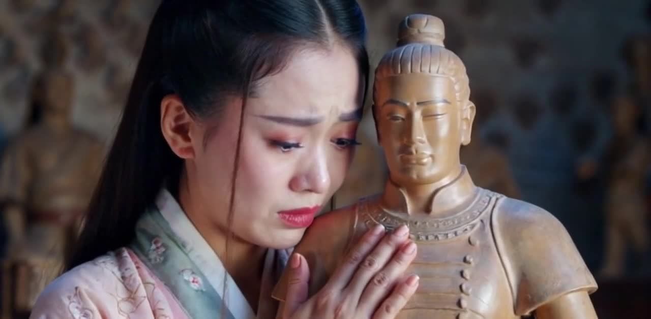 一名亚洲女性身穿汉服，抱着一尊兵马俑，面露悲伤，泪