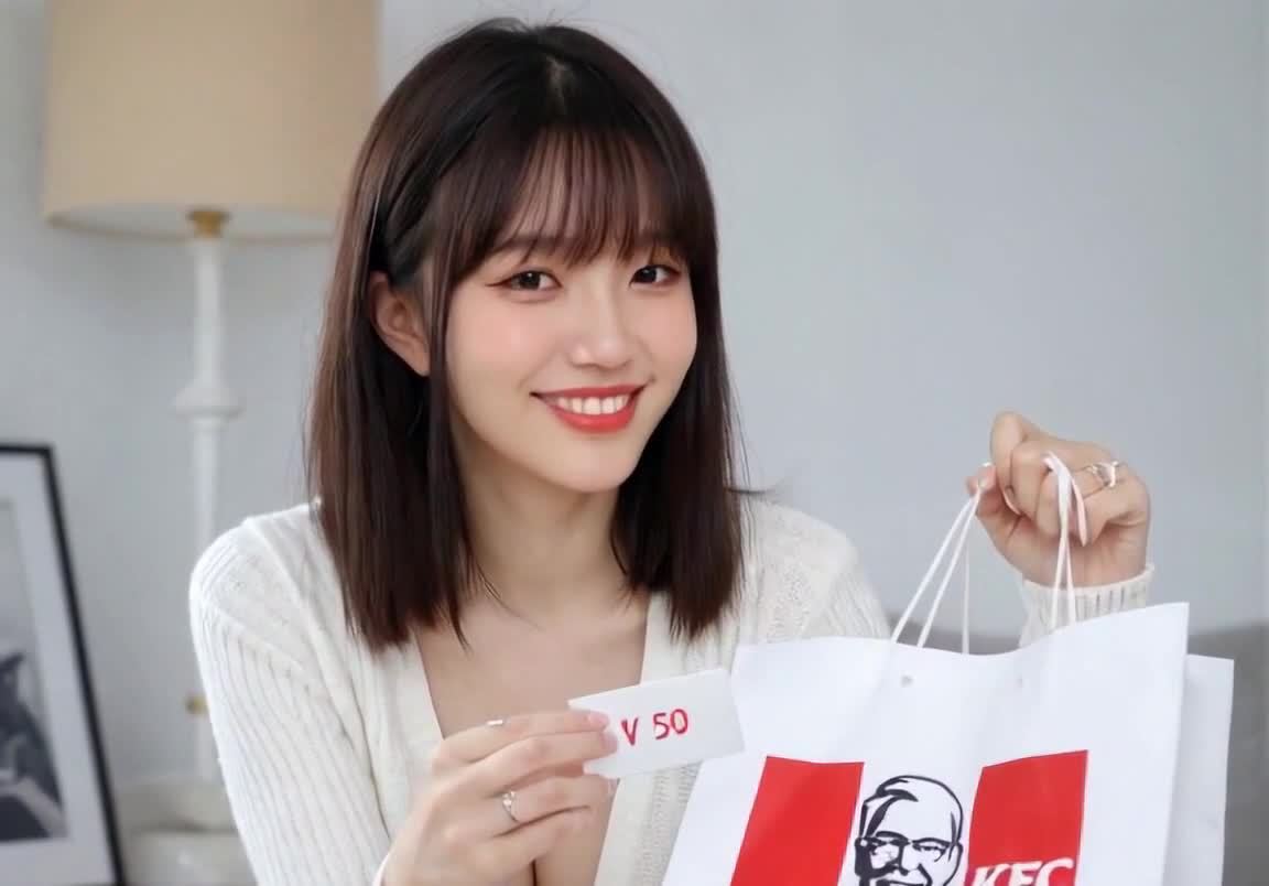 一位年轻女性坐在室内，她的头发是黑色的，穿着一件白