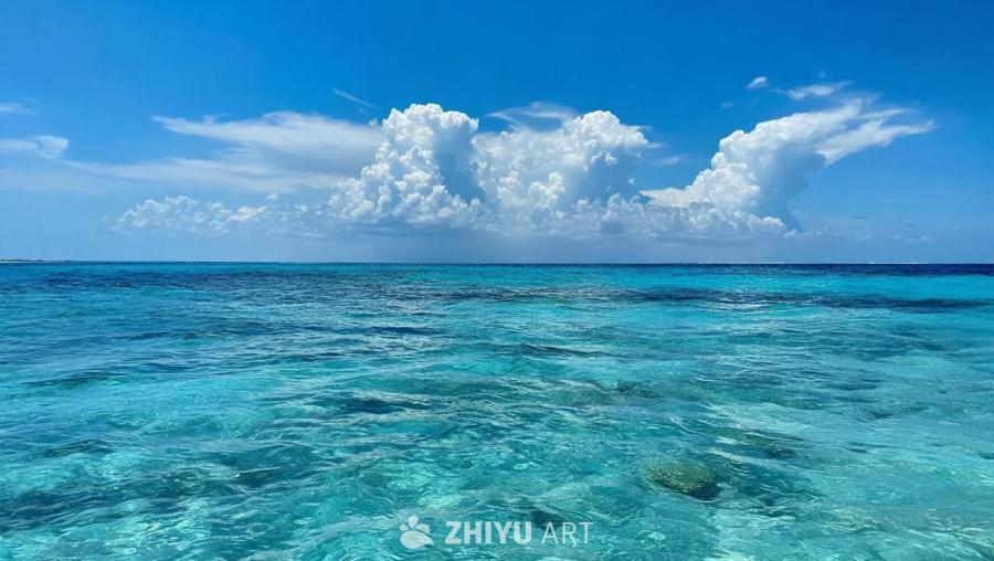 蓝天白云之下，是碧波荡漾的海面。海水呈现出多种蓝色