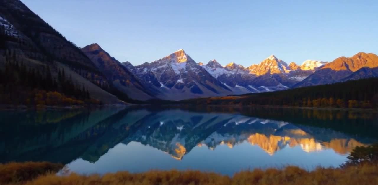 平静的湖泊，湖水清澈，倒映着远处的雪山。山峰被夕阳