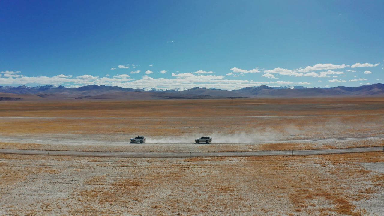 航拍越野车行驶在西藏无人区辽阔的草原上，车后扬起尘烟