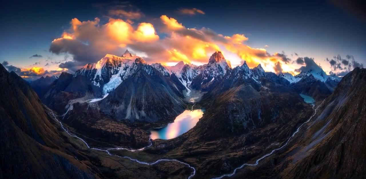 高耸的山峰连绵起伏，山峰顶部覆盖着积雪。天空被绚丽