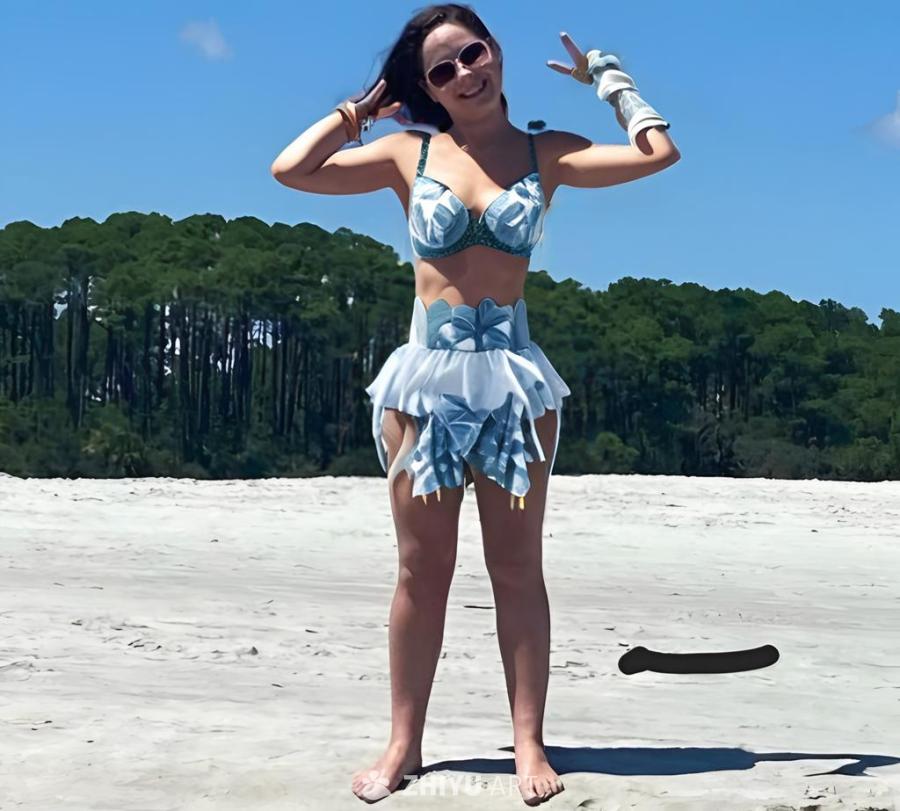 一名女子站在沙滩上，背景是绿色的树木和蓝色的天空。