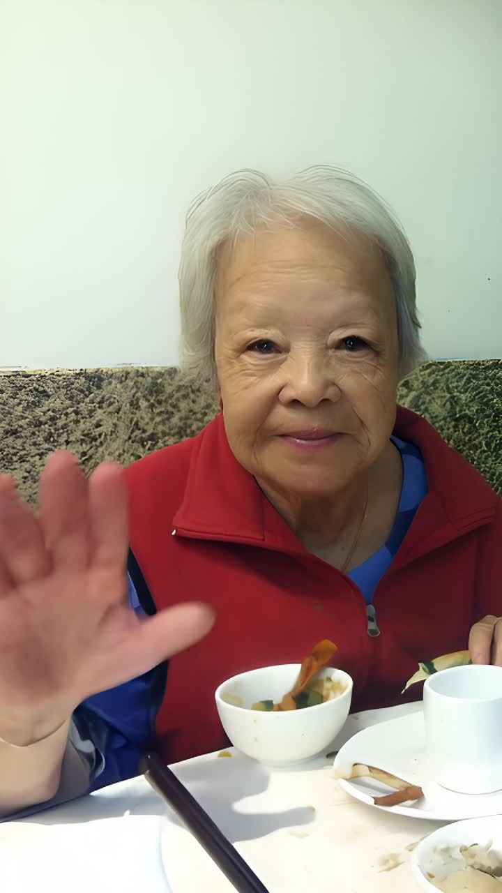 一位穿着红色马甲和蓝色印花衬衫的老年妇女，坐在一张