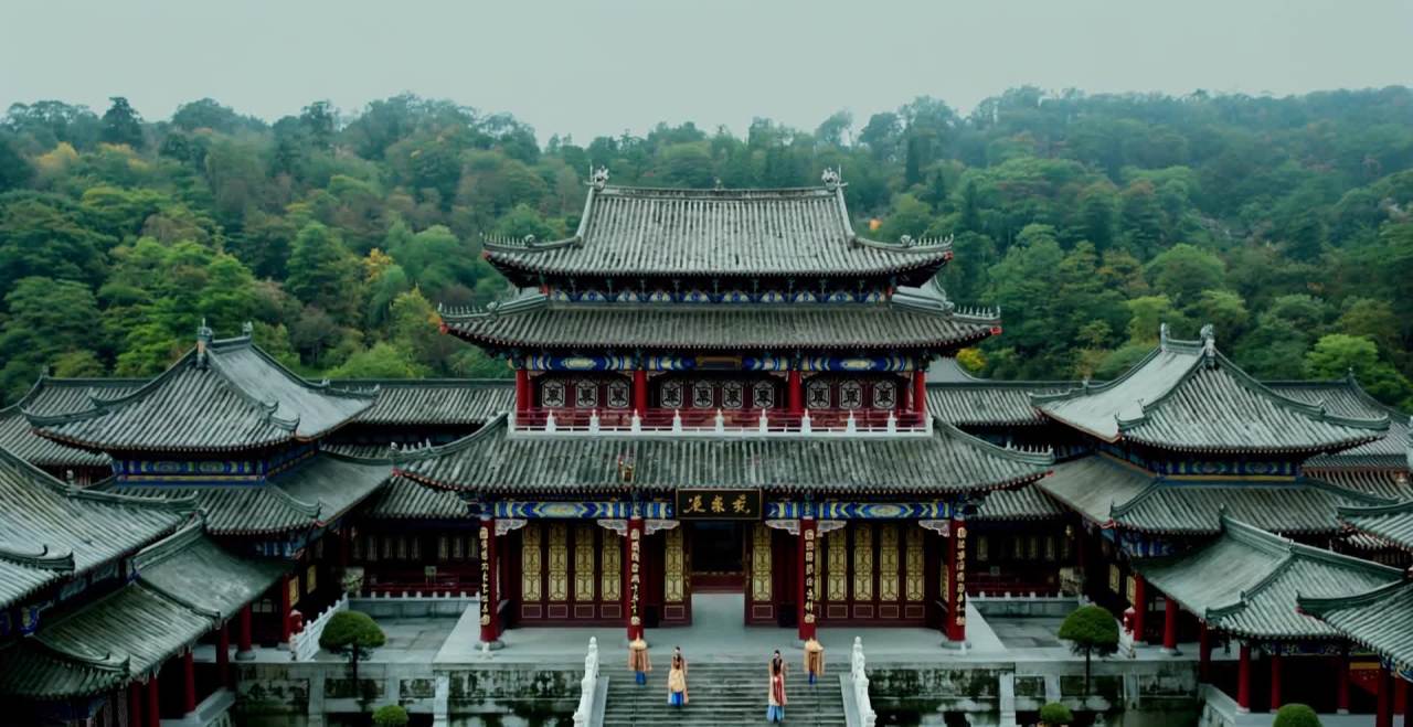 一座中式建筑，坐落于山脚下。建筑主体由灰色瓦片屋顶